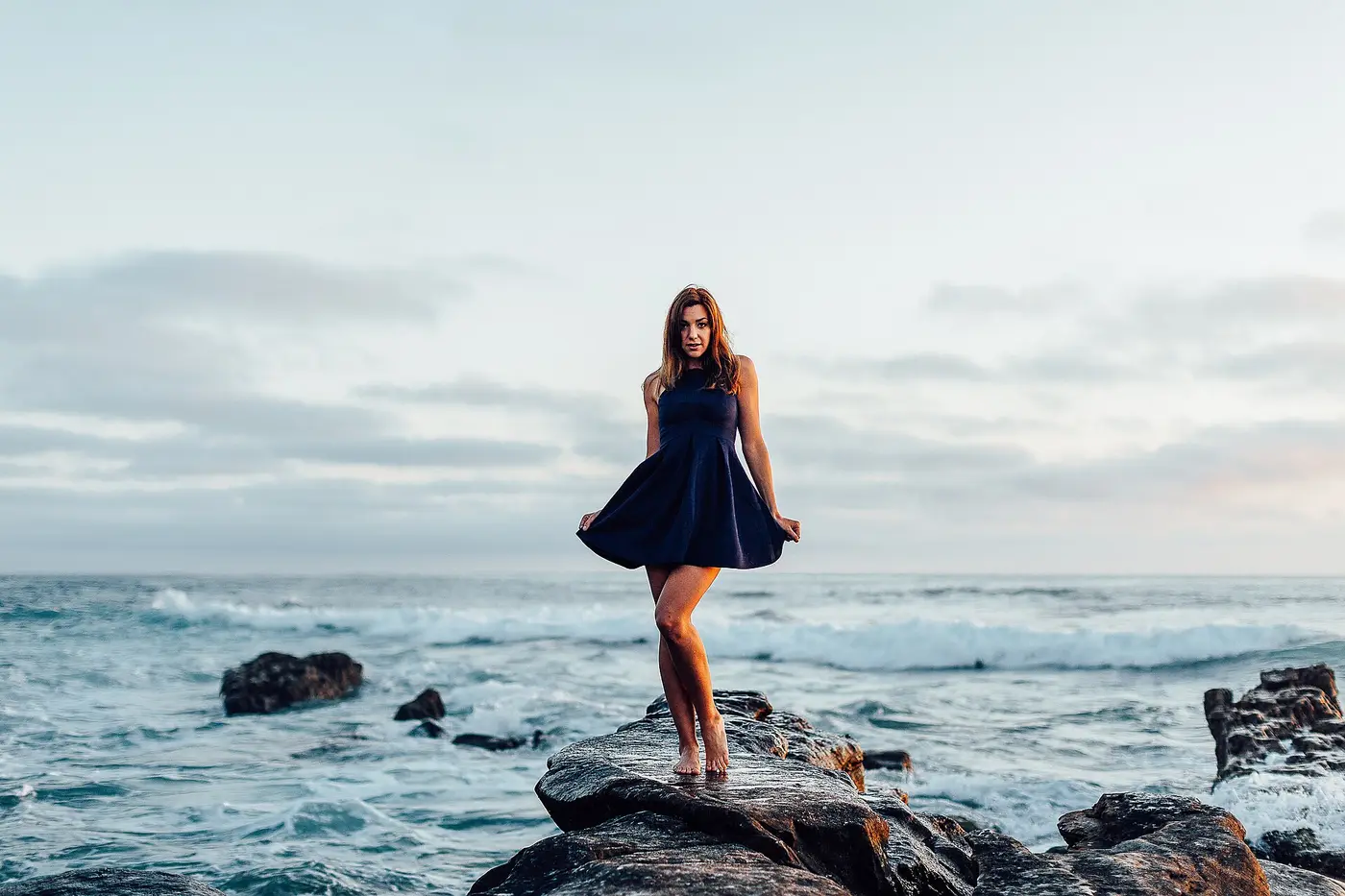 Femme en robe marine sur les rochers au bord de la mer